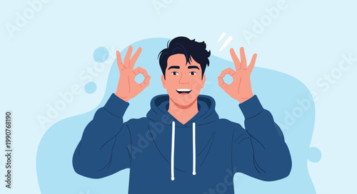 Cheerful young man in a blue hoodie showing the okay hand sign with both hands against a light blue background.