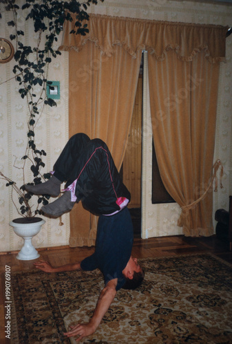 Teen hip hop breakdancer performing headstand freeze in living room, vintage 2000s home interior