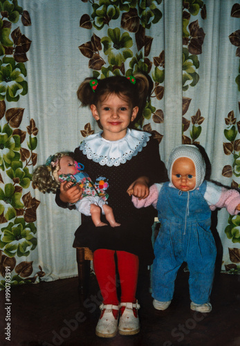 Authentic 1990s vintage family snapshot of smiling little girl holding dolls