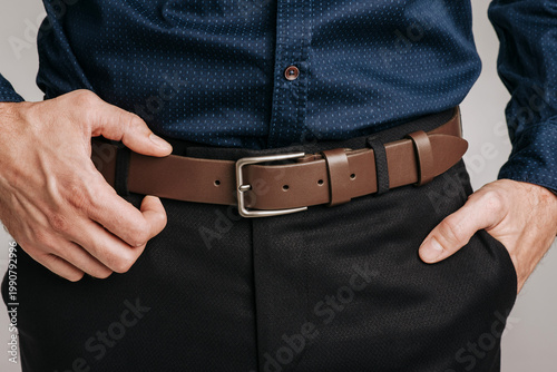 Obraz na płótnie Close-up of a man wearing a classic brown leather belt with a metal buckle on dark trousers and a blue shirt