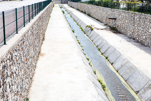 Narrow concrete water canal with stone retaining walls