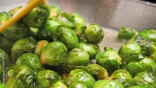Slow motion. Frying juicy fresh green Brussels sprouts in a frying pan with vegetable oil. Shiny sparkling Brussels sprouts shoots. Vegetarian hot dish. Vegetable food. Not frozen food.