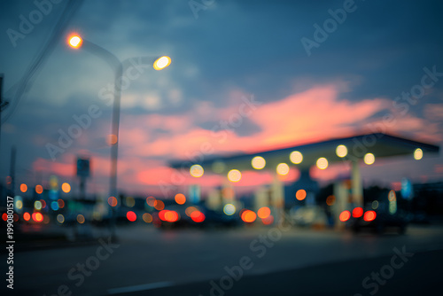 Blurred evening cityscape with vibrant sunset sky and illuminated gas station.