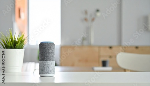 A smart speaker sits on a white table next to a potted plant.
