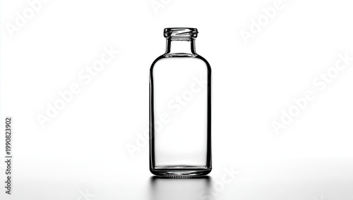 A clear glass bottle with a narrow neck and silver cap stands empty on a reflective surface