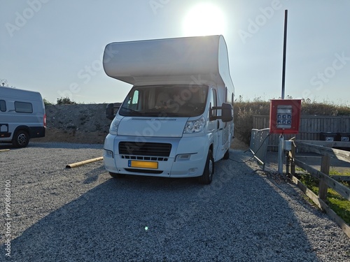 Motorhome parked at a campsite connected to an electricity hook-up under bright sunlight, representing travel, road trip lifestyle and outdoor living.