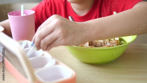 Close-up of young girl's hand seasoning a bowl of Thai chicken noodles with condiments in a restaurant, authentic street food culture concept
