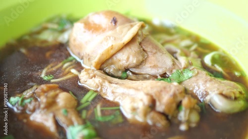 Close-up of braised chicken drumstick in rich brown broth soup, Thai street food noodle concept