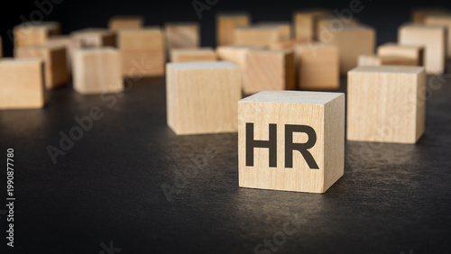 HR acronym on a wooden block. Blurred blank blocks on a dark background. Recruitment concept.