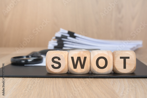 SWOT acronym on wooden blocks. Blurred document stack and magnifying glass. Business strategy concept.