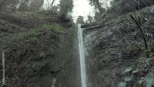 Tilt Down Along Tall Winter Waterfall On Rocky Cliff