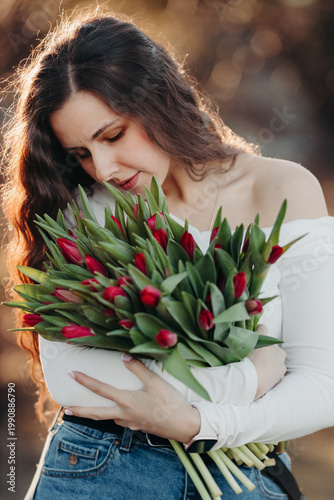Beautiful woman smiling with long brown hair hold tulips bouquet in hand. Close up woman portrait outdoor.
