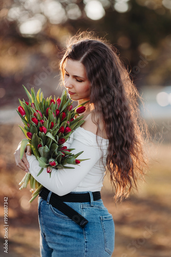 Beautiful woman smiling with long brown hair hold tulips bouquet in hand. Close up woman portrait outdoor.