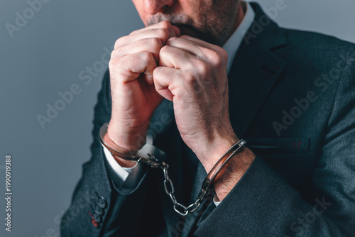 Handcuffed businessman with clenched hands, representing arrest, justice, financial crime, investigation, and loss of freedom in professional life.