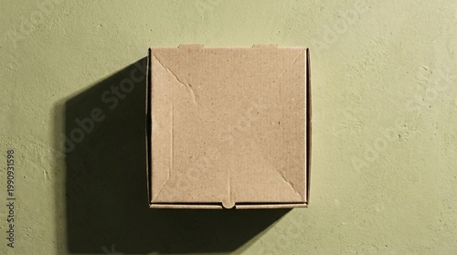 Top view mockup of a square kraft paper pizza box on green textured background with dramatic shadow