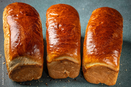 Bild auf Leinwand Three golden brioche loaves on dark background