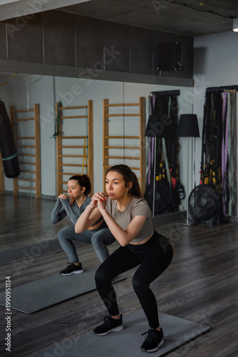 Schilderij op canvas Women perform squats in a fitness studio with exercise mats and gym equipment in