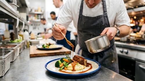 Professional chef plating gourmet meat dish in restaurant kitchen, culinary expert garnishing dinner plate with sauce, busy commercial kitchen scene