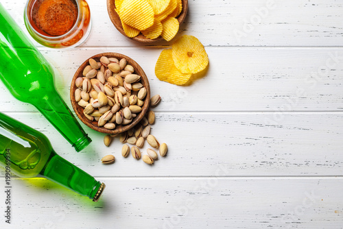 Beer bottles with pistachios and chips on white table