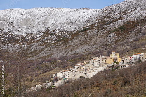 mountain landscape with snow and trees and the village of coursegoules, southern france