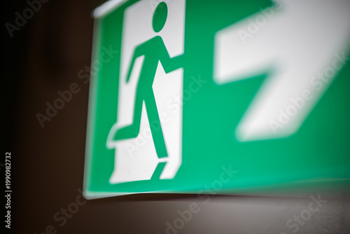 Photography Close-up of green emergency exit sign with running figure and directional arrow