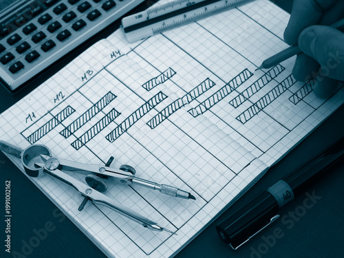 Hand drawing a project schedule chart in a notebook with technical drafting tools
