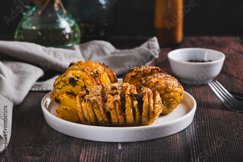 Foto Baked Hasselback potatoes with cheese, garlic and herbs on a plate on the table