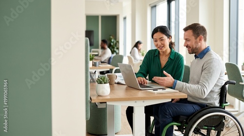 Professional Asian woman and Caucasian man in wheelchair collaborating on a project using a laptop in a bright, modern, inclusive office environment