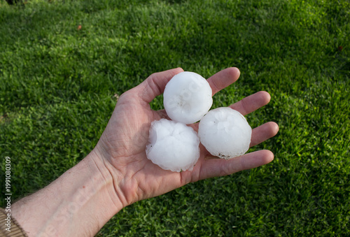 Foto A person's hand holds three large hailstones, each over two inches in diameter