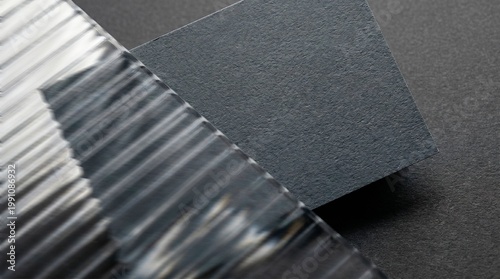 A minimalist and sophisticated composition featuring a black textured paper business card under a fluted glass pane, creating an elegant play of light, shadow, and transparency for branding presentati