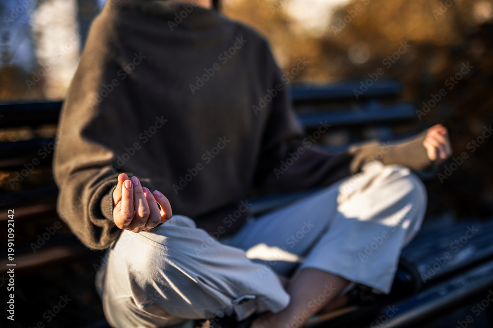 Fototapeta premium Close up of hands and legs in meditation pose on park bench