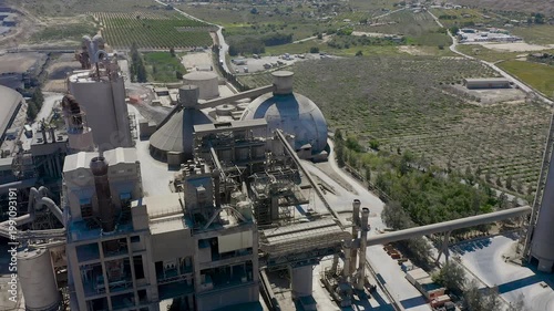 Aerial view of cement manufacturing plant in Alicante, Spain. Industrial complex with silos, conveyor systems and production facilities surrounded by agricultural landscape near Mediterranean coast. 