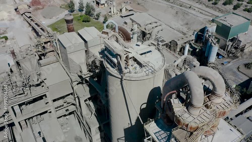 Aerial view of cement manufacturing plant in Alicante, Spain. Industrial complex with silos, conveyor systems and production facilities surrounded by agricultural landscape near Mediterranean coast. 