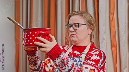 woman wearing a red  Christmas sweater and apron is laughing with horror while holding red polka dot pot, showing joyful lifestyle associated with cooking and creating a fun moment in the home kitchen