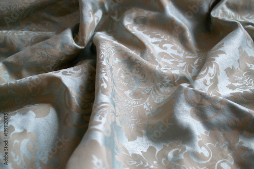 Closeup of elegant blue satin fabric with classic floral damask pattern and soft folds. Shiny textile surface used for luxury interior or fashion design background.