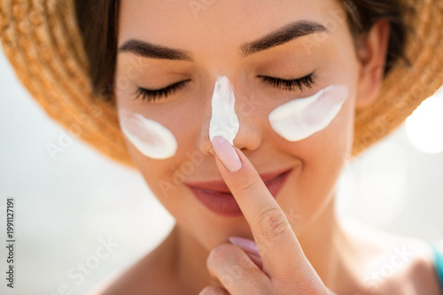 фотографія Beautiful woman applying sunscreen on nose with finger smiling with closed eyes
