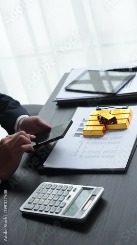 Gold investment Concept. Businessman using phone checking on gold price for working on financial planning and gold investment analysis with bullion on desk.