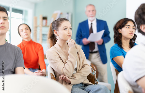 Young girls and guys audience listen to lecture, mature man teacher in background. Social projects for young people. Prevention of addictive behavior, information support for youth in bullying