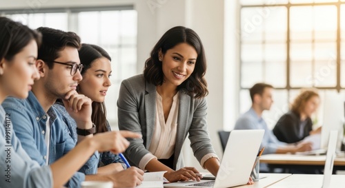 A group of diverse colleagues engaged in a collaborative meeting around a laptop in a modern office setting.