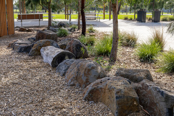A row of natural basalt and granite boulders used as landscape edging along a garden bed border in a suburban park in Australia, with native ornamental grasses, woodchip mulch,  eucalyptus trees