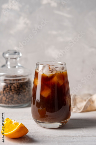 Coffee with orange juice bumble in a tall glass with ice on a light background with coffee beans, fruits and morning shadows