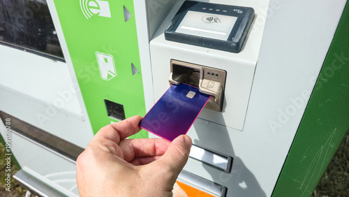 Hand inserting purple payment card into reader, electronic transaction, kiosk.