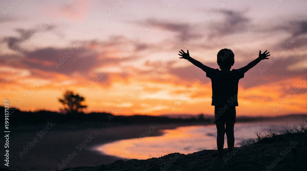 Fototapeta premium Silhouette of a young child with arms outstretched at sunset.