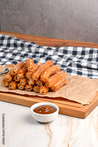 Obraz na plátně Tower of freshly fried artisanal churros on a rustic wooden board and waxed pape