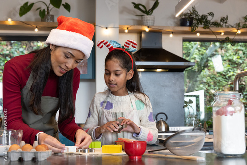 Indian mother and daughter in Santa hat and fun headband baking cookie cutters on kitchen counter