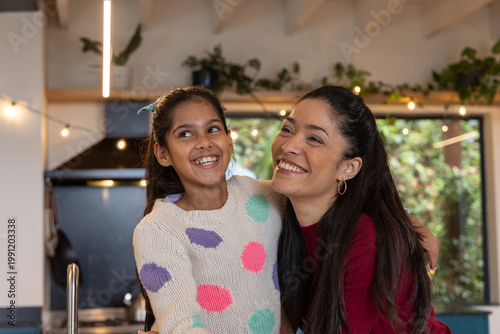 Asian mother and child hugging and smiling in kitchen, child wearing polka-dot sweater near faucet
