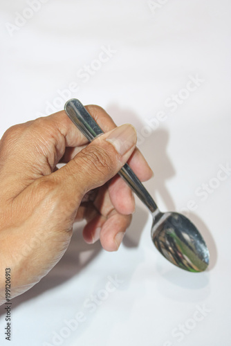 Hand holds silver spoon against plain white background