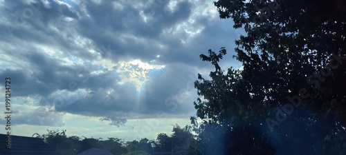 Dramatic sky with sunbeams breaking through clouds and silhouetted trees in a rural landscape