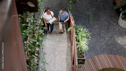 Vertical video: 2 IT staff with box on atrium steps tapping tablet showing overlay confirming route