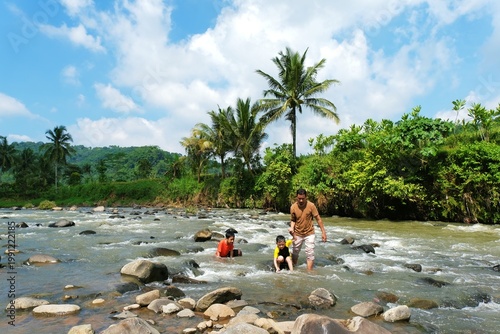Bilde på lerret Father and son enjoying playful moment in shallow river surrounded by tropical landscape creating joyful outdoor family lifestyle scene